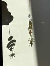 Hanging ornament featuring a clear vintage glass crystal atop three gold geometric shapes, casting a distinct shadow on a light background.