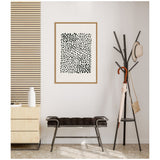 Framed abstract wall art featuring irregular black dots on white, hung above a dark cushioned bench between a striped wood panel and a black coat rack with a hat and umbrella.