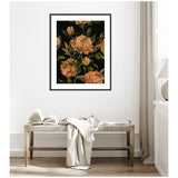Framed floral art with peach-colored flowers and green leaves on a black background, hanging above a wooden bench with a draped light fabric and open book.