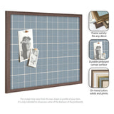 Rectangular light blue fabric pinboard with white grid lines and dark wood frame, displaying two black-and-white photos pinned with copper thumbtacks.