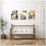 Three framed abstract canvas artworks featuring beige, black, white, olive green, and red accents, hung symmetrically above a wooden bench with white cushions in a bright room.