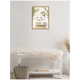 Framed canvas of three penguins in a cream clawfoot bathtub surrounded by green palm leaves on a white tiled wall, hanging above a white bench with a fluffy throw.
