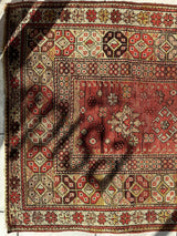 Rectangular antique Turkish wool prayer rug with a distressed red central field and intricate geometric border patterns in cream, red, and black tones, partially shadowed.