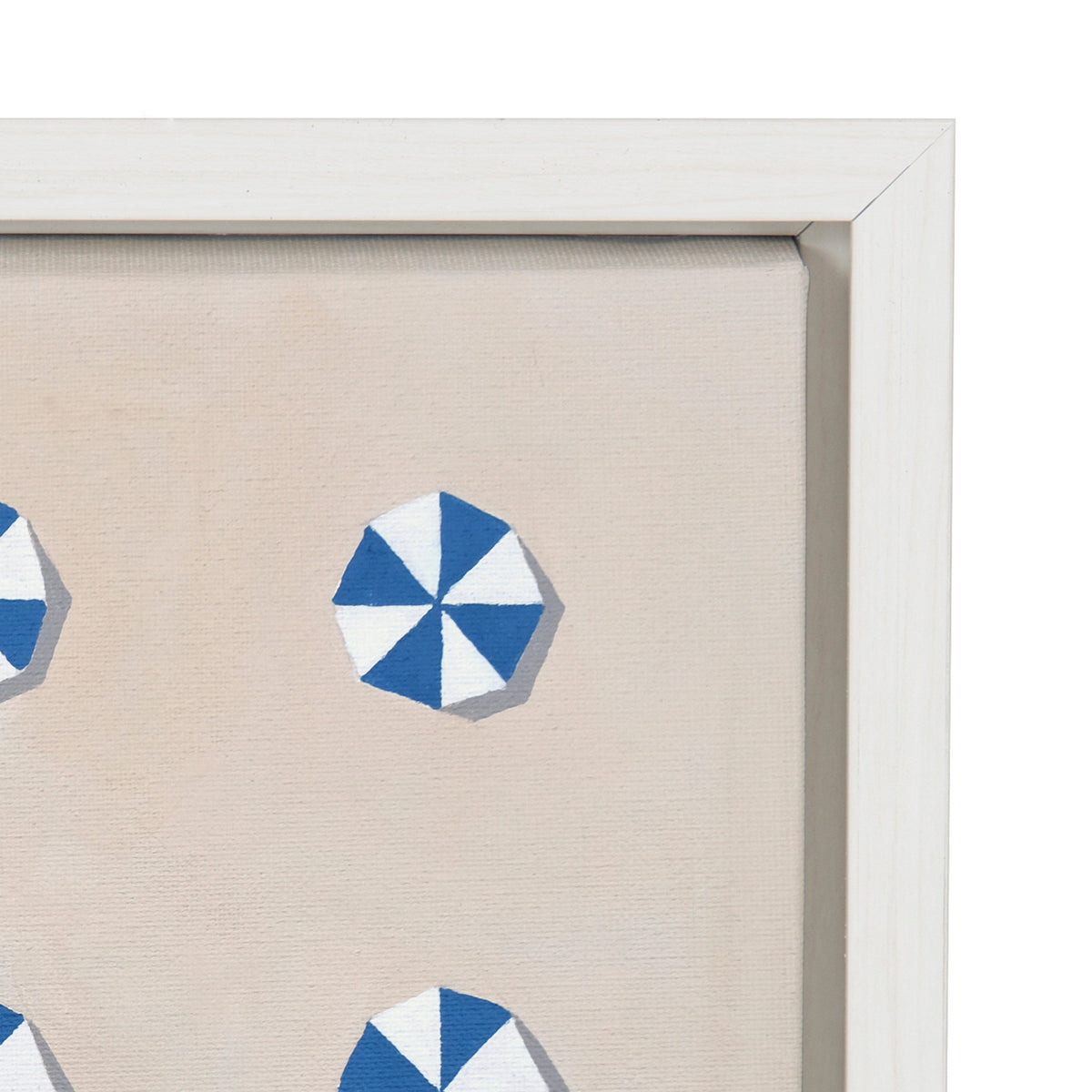 Close-up of a framed canvas artwork showing blue and white geometric pinwheel shapes on a beige background with a white wooden frame.