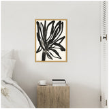 Black abstract botanical painting with bold brushstrokes on white background, framed in light wood, hanging above a rustic wooden bedside table with books and a white cup.