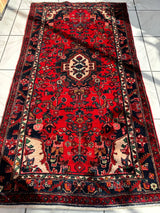 Rectangular hand-knotted Persian Hamadan wool rug featuring a red field with intricate floral motifs and a central cream medallion, bordered by navy blue and cream patterns.