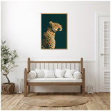 Framed canvas print of a gilded cheetah profile on a dark green background, hanging above a wooden bench with white cushions in a minimalist room.