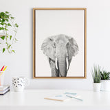 Framed black-and-white elephant portrait by Simon Te, centered on a white wall above a minimalist white desk with plants and stationery.