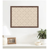 Beige pinboard with a green lattice pattern enclosed in a dark wooden frame, hanging on a white wall above a white shelf with a lamp, photo frame, and potted plant.