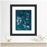 Framed aerial artwork of six humpback whales swimming in deep blue ocean water, displayed above a minimalist wooden shelf with white decor.