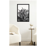 Black and white framed photograph of tall palm tree fronds with detailed leaves against a white wall, placed between two cream upholstered chairs and a brass side table with a small white vase