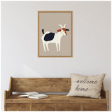 Minimalist cartoon-style goat illustration with white body, black patch, brown and black head, framed on beige wall above wooden bench with "welcome home" pillow and open book.