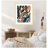 Abstract framed wall art featuring colorful overlapping leaves in mustard, teal, coral, and olive tones on a light background, hanging above a cozy beige and white bed.
