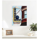 Framed canvas print of a vintage neon sign reading 'Pardon My French' with a curved brick building in the background, displayed on a white wall above a minimalist shelf.
