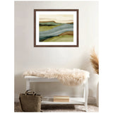 Abstract landscape art print in earthy tones of green, beige, and brown framed above a white wooden bench with a beige faux fur throw and brown bag underneath.