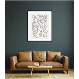 Abstract black continuous line drawing with organic shapes in white mat and black frame on a dark green wall above a brown leather sofa with a wooden coffee table and decorative glass vase.