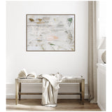 Abstract framed canvas with soft white, beige, and muted green brushstrokes above a wooden bench with a draped cream fabric and open book in a neutral-toned room.