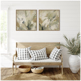 Two framed abstract floral paintings in soft green and beige tones hang above a wooden bench with white and gray checkered cushions, beside a large white vase with tall greenery.