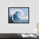Abstract coastal ocean wave print with swirling blues and white foam in a black frame, hanging above a dark desk with an open book, glasses, and beige lamp.