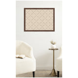 Rectangular wall pinboard with a beige surface and dark brown lattice grid pattern, framed in dark wood, hanging above a brass pedestal table with a white vase and two white cushioned chairs.
