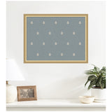 Rectangular blue botanical block print with evenly spaced small beige leaf motifs framed in light wood, displayed above a white surface with a lamp and potted plant.