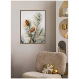 Framed canvas art of pine branches with two brown pinecones against a soft white background, displayed on a beige wall above a textured cream chair with a wrapped gift and gold ornament.