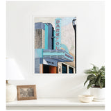 Framed canvas print of a retro theater facade with teal and pink vertical 'DARE YOU' sign and marquee reading 'DOUBLE DOG', hanging on white wall above a table with lamp, photo frame, and potted plant.
