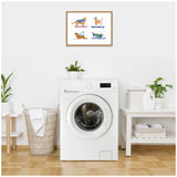 Framed illustration of four cartoon dogs in colorful sweaters skiing, mounted above a white front-load washing machine in a minimalist laundry room setting.