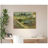 Vincent van Gogh's Garden at Arles painting featuring vibrant green plants and yellow flowers, framed above a wooden desk with books and a plant nearby