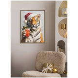 Framed canvas of a tiger wearing a red Santa hat, holding a festive cocktail glass with a holly garnish, hung on a light gray wall above a beige textured chair with gold-wrapped gift.