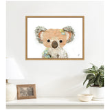 Framed canvas print of a stylized koala with textured grey ears and pastel floral accents, hung above a white shelf with a lamp, photo frame, and plants.