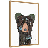 Portrait of a bear made from natural bark, leaves, and small blue flowers on a white background with a light wooden frame