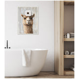 Framed canvas art of a brown alpaca with a roll of toilet paper on its head, hung on a white wall above a white freestanding bathtub in a modern bathroom.