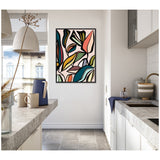 Abstract framed wall art with bold black outlines and colorful organic shapes resembling leaves in shades of teal, pink, olive, and rust in a bright kitchen corner.