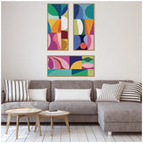 Three framed abstract canvas panels with bold geometric shapes in blue, green, pink, and orange above a gray sectional sofa with striped and solid pillows in a light, minimalist living room.