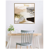 Abstract framed wall art with soft beige, gray, and gold tones above a minimalist wooden desk with a potted plant and a gray wooden chair.