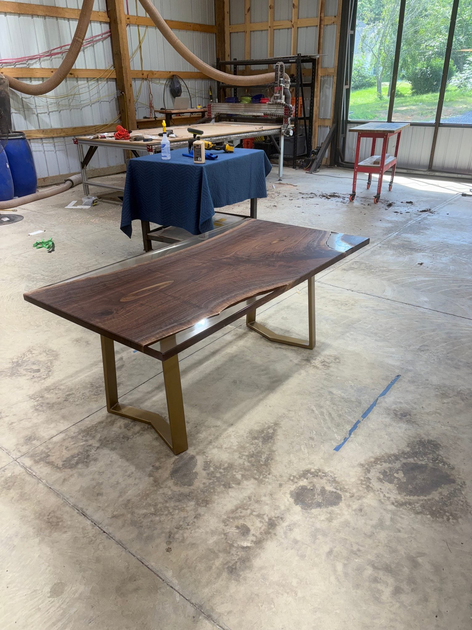Handcrafted walnut slab table with clear resin finish and gold legs in a workshop setting