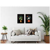 Two framed canvas art pieces above a white sofa, featuring stylized yellow and orange vases with colorful floral arrangements on black backgrounds in a modern living room.