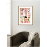 Framed wall art displaying vintage pink-themed matchbox illustrations with varied designs and text, hanging above a dark upholstered armchair with a knitted throw.
