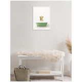 Framed canvas showing a lion cub sitting in a vintage green bathtub on a floor with multicolored square tiles, hanging on a plain light wall above a white bench draped with a soft fur throw.