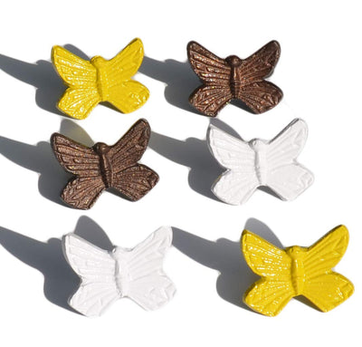 Set of six Vibhsa butterfly napkin rings in antique copper, yellow, and white finishes on a kitchen table.