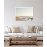 Neutral-toned living room with a light beige sofa, striped and solid pillows, wooden coffee table with books and cups, and a coastal landscape framed canvas above.