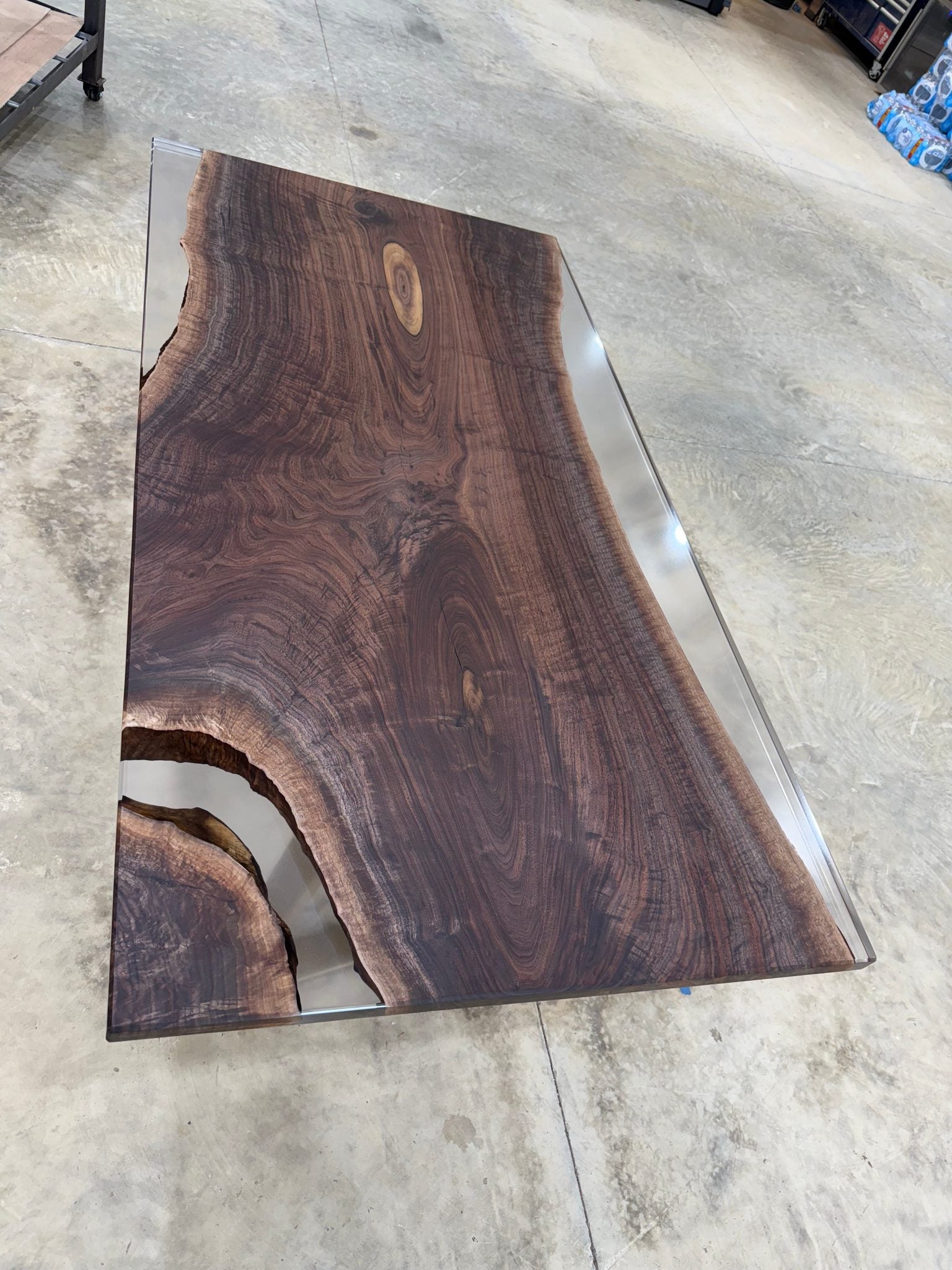 Handcrafted walnut slab table with clear resin finish and gold legs in a workshop setting