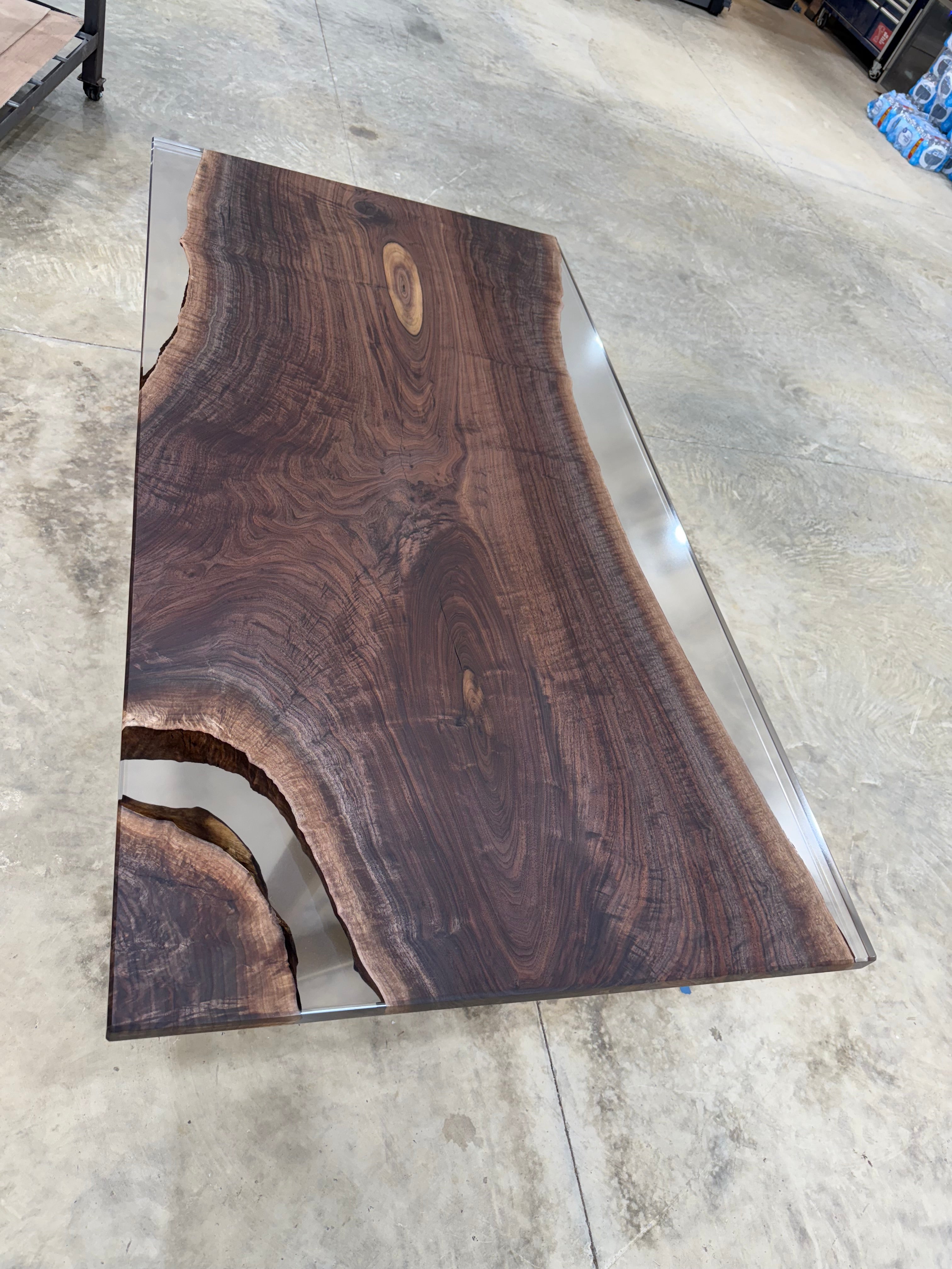 Handcrafted walnut slab table with clear resin finish and gold legs in a workshop setting