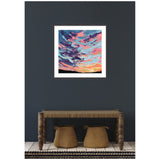 Framed painting of a colorful sunset sky with purples, blues, pinks, and oranges above a dark silhouetted horizon, displayed on a dark gray wall above a wooden bench and two woven baskets.