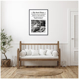 Black-and-white framed artwork styled as a vintage newspaper page titled The Good Times, featuring a photo of a relaxed woman reclining outdoors, hung above a wooden bench with white cushions in a minimalist room.