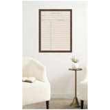 Framed linen pinboard styled as a vintage library card with brown wooden frame, displayed on a white wall above a brass side table and cream upholstered chairs.
