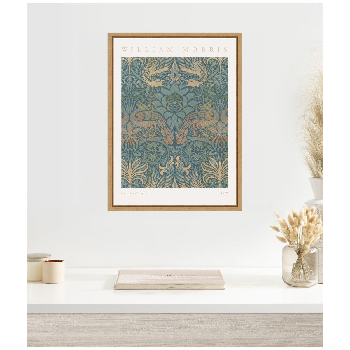 Framed William Morris 1878 Peacock and Dragon artwork with intricate blue and gold botanical and bird motifs, hung on a white wall above a minimalist desk setup.