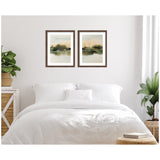 Two framed abstract landscape prints with soft green, beige, and black hues hang side by side above a white bed in a minimalist bedroom with plants.