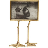 Gold lacquered picture frame with two duck feet as support, holding a 13x18 cm photo, shown on a neutral surface.